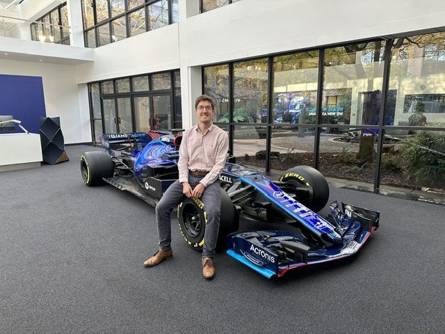 James Crook sitting on the front wheel of a Williams Formula 1 car